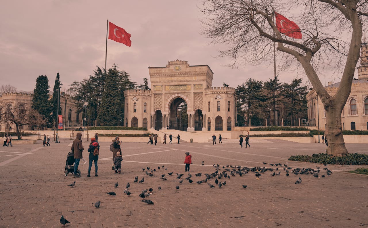 People enjoying a warm day at Istanbul's iconic university gate with pigeons around.