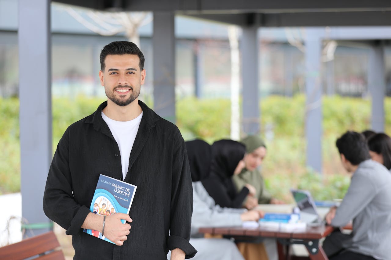 Confident university student holding a language textbook with friends studying in the background.